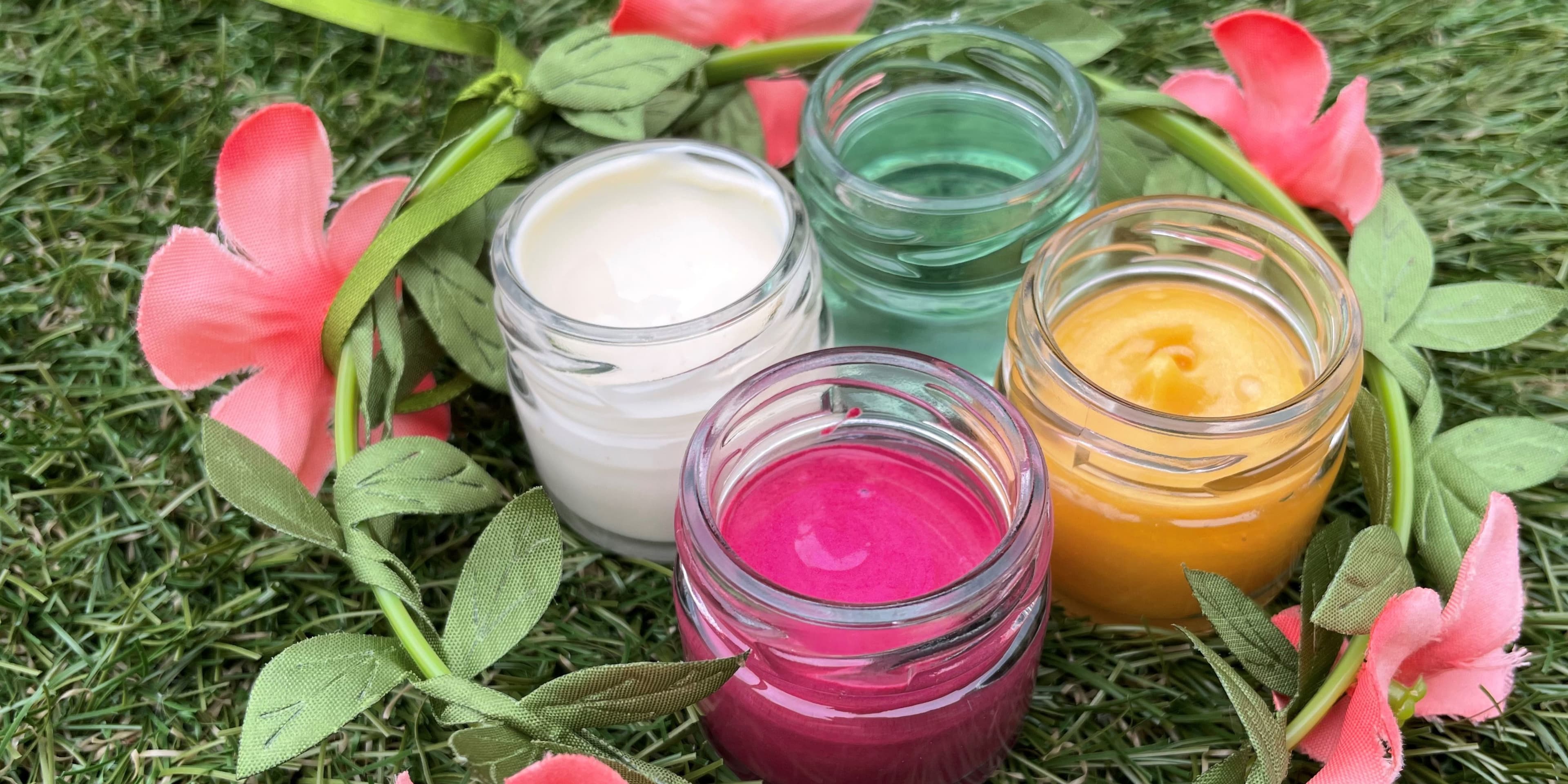 4 formulations (1 pink, 1 gold, 1 green, and 1 white) in jars on a grass background