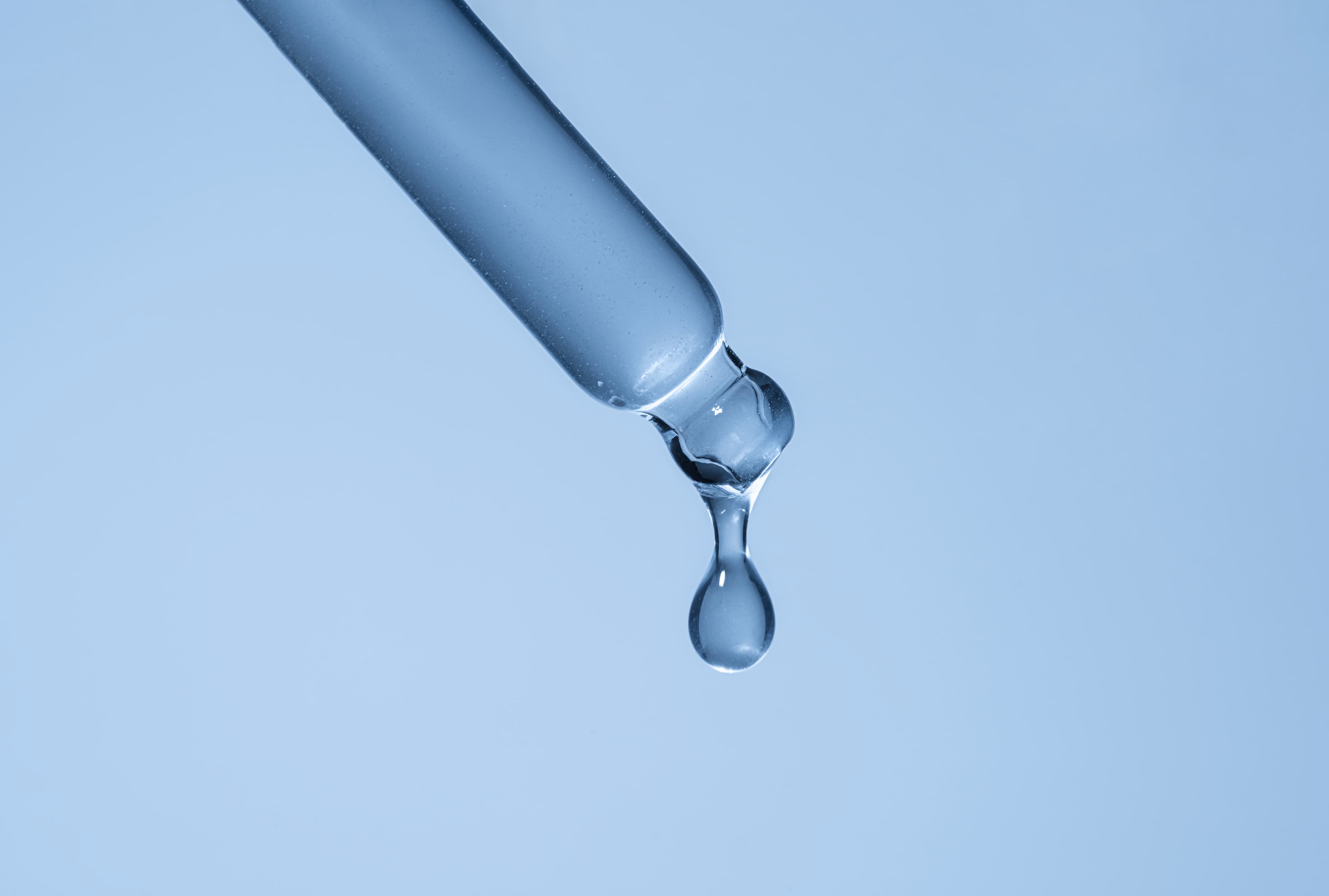 Liquid being dropped from a dropper on a light blue background