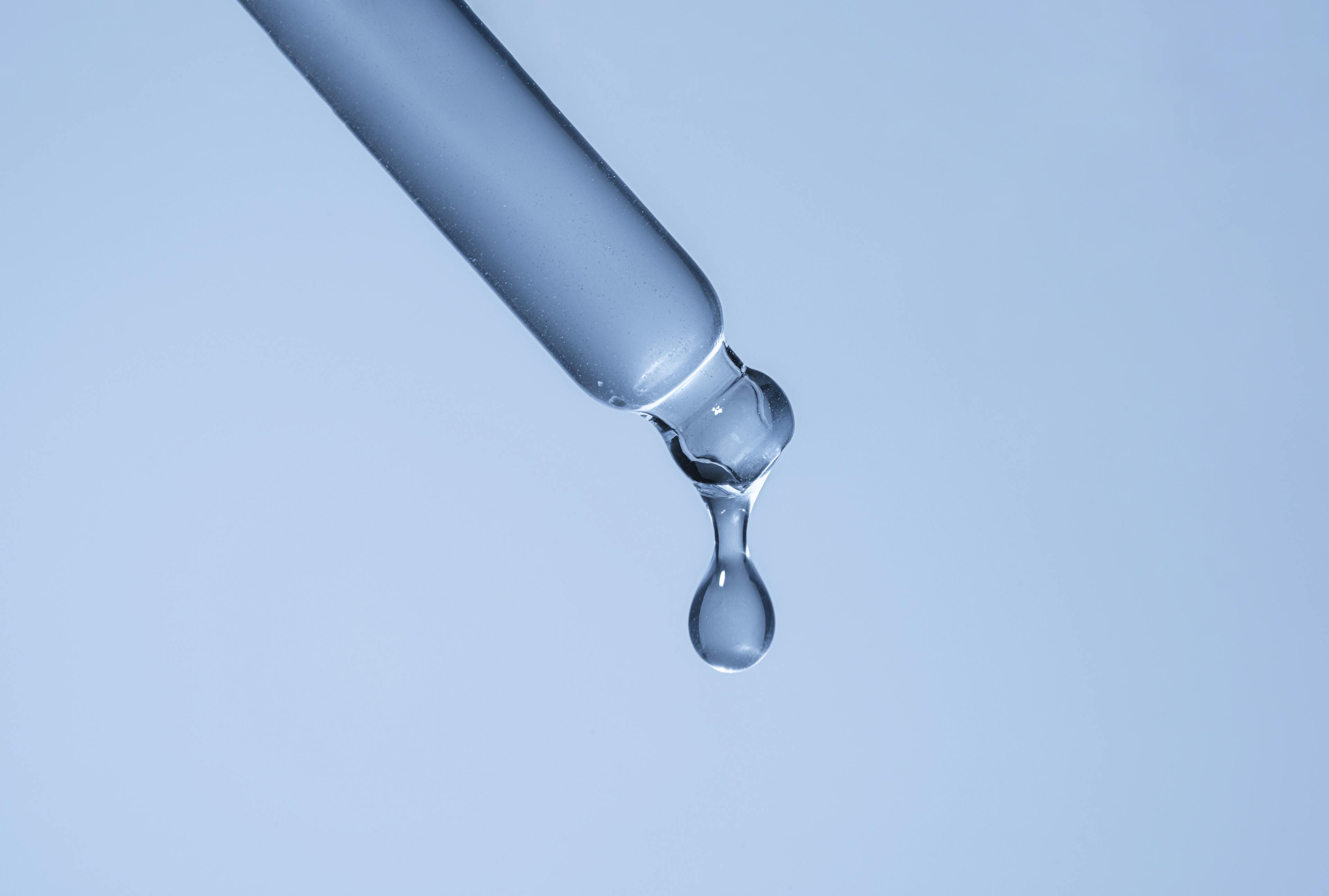 Liquid being dropped from a dropper on a light blue background