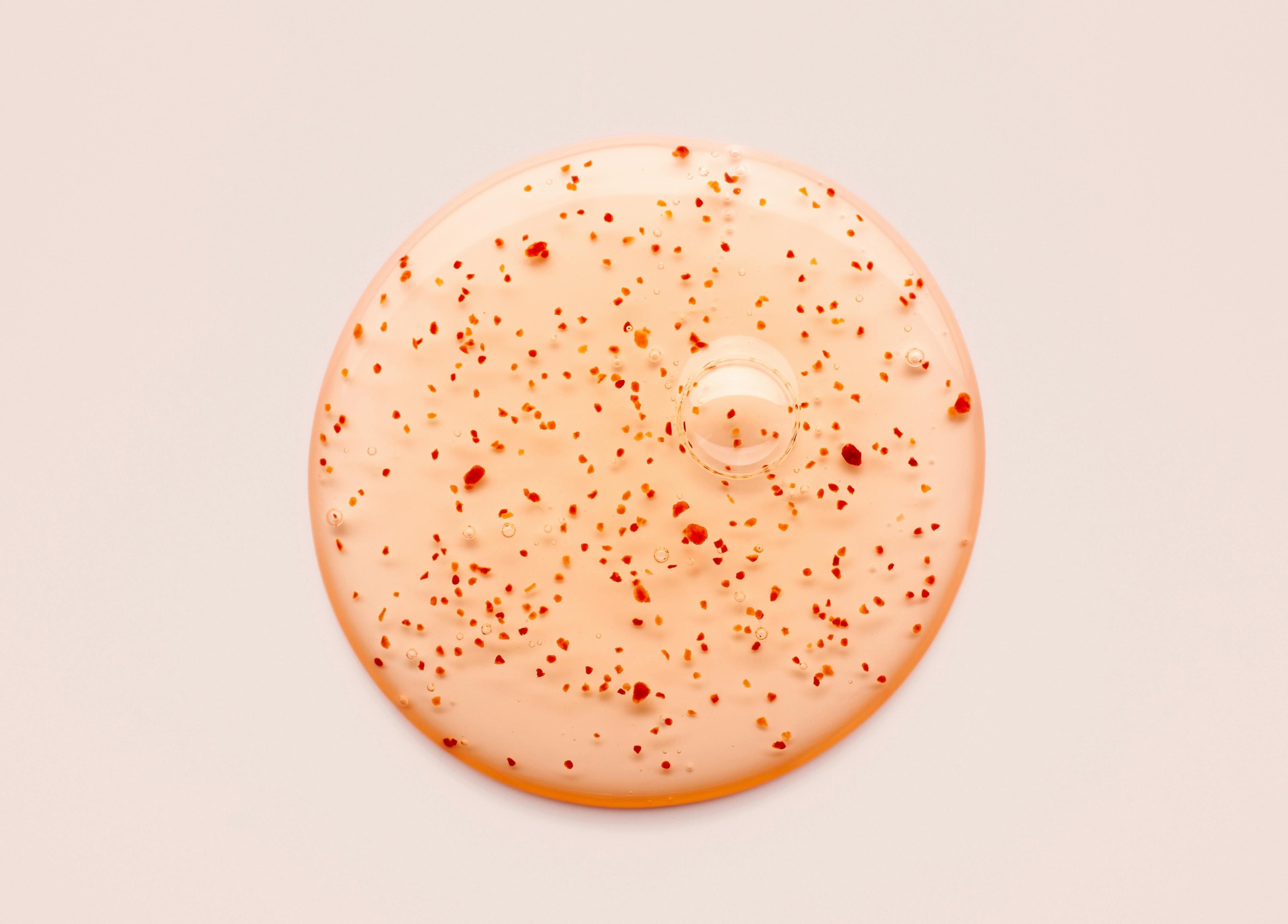 Light orange gel with red suspended particles on a pale pink background