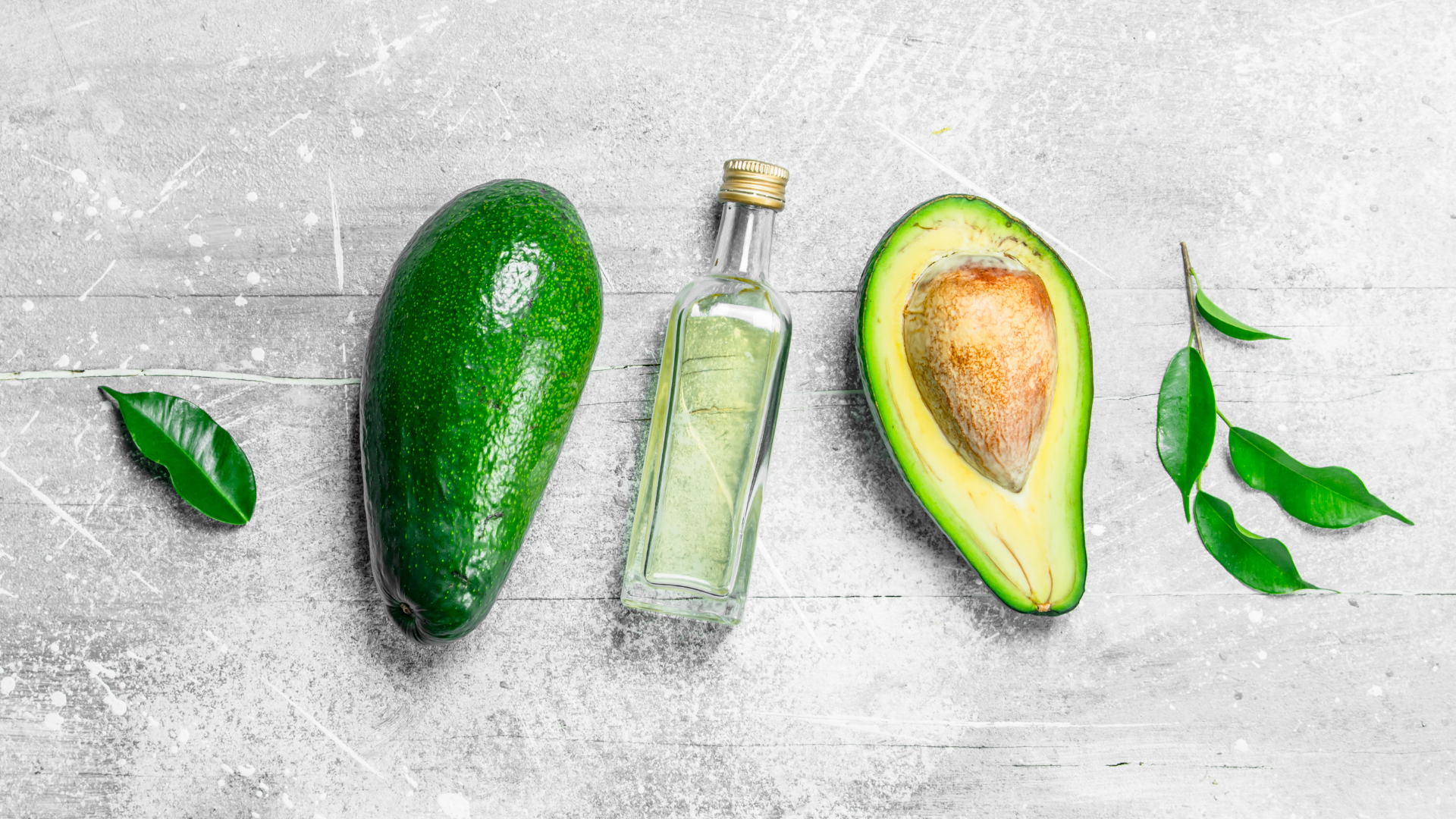 Oil bottle surrounded by avocados and leaves